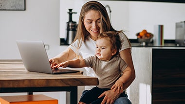 Young mother working from home on laptop with her little son