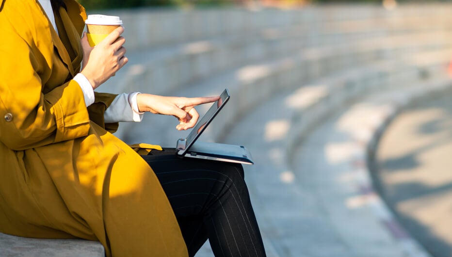 Woman checking laptop outside with coffee