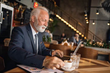 Carefree senior businessman working from a cafe in formalwear during a coffee break.